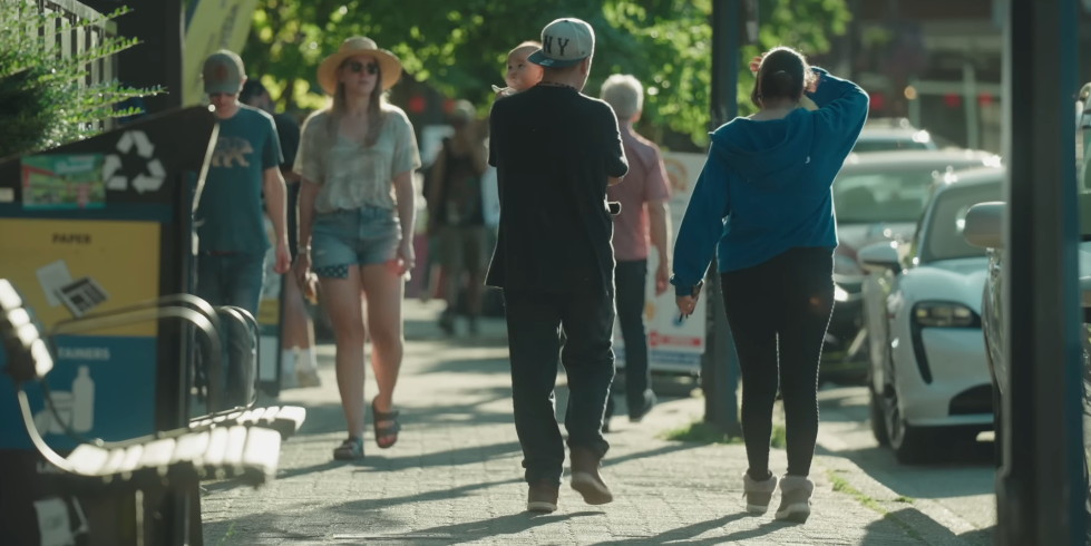 A busy street scene with people walking and cars parked along the side.