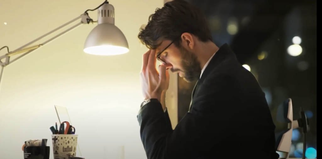 A man in a suit sitting at his desk, looking stressed and overwhelmed, symbolizing work-related non-productivity.